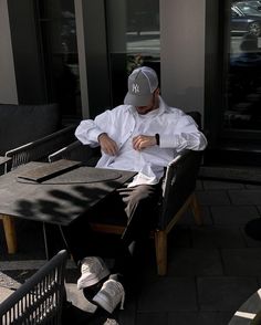 a man sitting at a table in front of a building with his hands on his knees