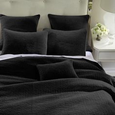 a bed with grey linens and pillows in a white room next to a night stand