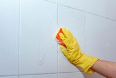 a person in yellow gloves and rubber gloves cleaning a white tile wall with a sponge