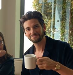 a man and woman sitting at a table with coffee in front of them, smiling