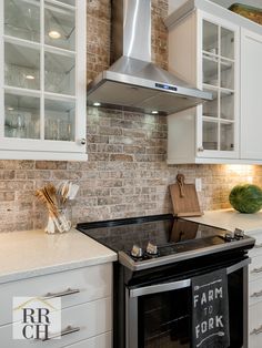 a kitchen with white cabinets and an oven in the center, surrounded by brick walls