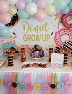 a table topped with donuts and cake next to balloon garlands on the wall