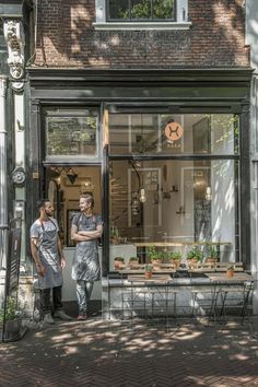 two men standing in front of a store window with potted plants on the windowsill