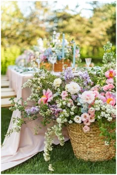 a basket filled with lots of flowers on top of a grass covered field next to a table