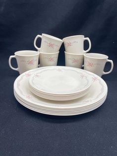 a set of six white cups and saucers with pink flowers on the rims