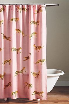 a pink shower curtain with giraffes printed on it and a white bath tub