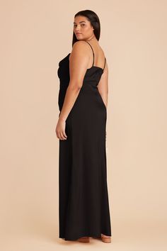 a woman is wearing a black dress with one shoulder and an open back, standing in front of a beige background