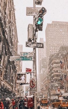 people are walking down the street in the snow with traffic lights and signs on poles