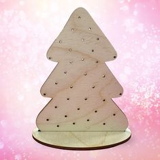 a wooden cutout of a christmas tree on a pink background with snow flakes