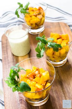 three glass bowls filled with food on top of a wooden cutting board