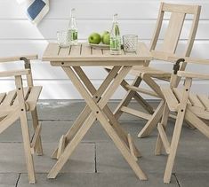 an outdoor table with four chairs and two green apples on the table next to it