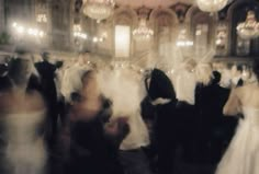 blurry photograph of people in formal wear dancing at a wedding reception with chandeliers hanging from the ceiling