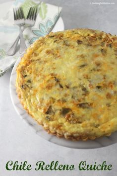 a cheesy quiche on a white plate with a fork and napkin in the background