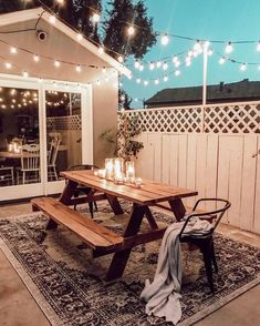 a picnic table with candles on it in front of a patio area that has lights strung from the roof