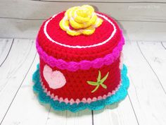 a red crocheted hat with a flower on top sitting on a white wooden floor