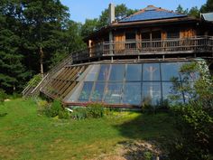 a wooden house with large glass windows in the middle of a grassy area surrounded by trees