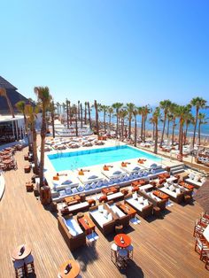 an outdoor swimming pool surrounded by lounge chairs and palm trees with the ocean in the background