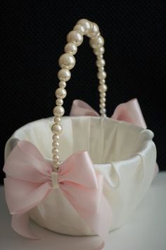 a white basket with pearls and a pink bow on the handle is sitting in front of a black background