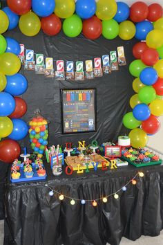 a birthday party with balloons and toys on the table in front of a black backdrop