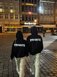 two people in black hoodies walking down a street at night with the words private written on them