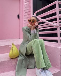 a woman sitting on the steps in front of a pink building with her hand under her chin