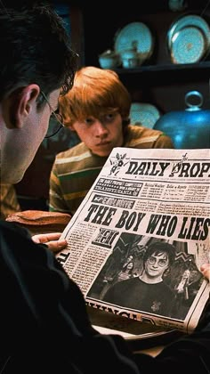 two people sitting at a table looking at a newspaper with an image of harry potter on it