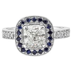 a cushion cut diamond surrounded by blue and white sapphires in an 18k white gold ring