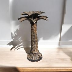 a decorative vase sitting on top of a wooden table next to a wall with a shadow cast on it