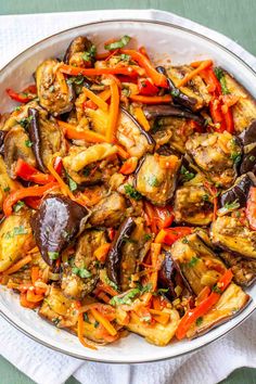 a white bowl filled with eggplant, carrots and other vegetables on top of a napkin