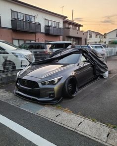 a grey sports car parked in a parking lot next to a building with cars behind it