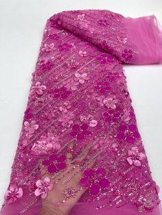 a person's hand is touching the pink fabric with flowers on it, which has been sequins and beads