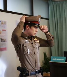 a man in uniform adjusts his hat while standing next to a desk with papers on it