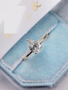 an engagement ring with a pear shaped diamond sits in a blue velvet box on a white background