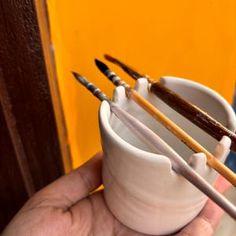 a person holding a cup with some paintbrushes in it and two other brushes