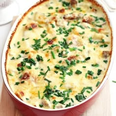 a casserole dish with meat and vegetables in it on a wooden table next to a bowl of tomatoes