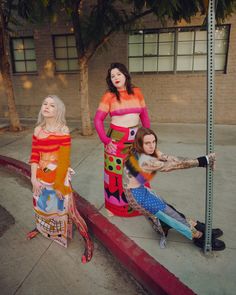 three women dressed in costumes posing on the side walk next to a street sign and tree