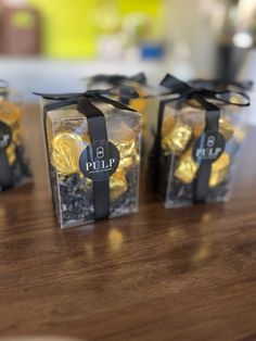 four small clear boxes filled with chocolates on top of a wooden table