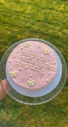 a pink frosted birthday cake sitting on top of a glass plate in the grass