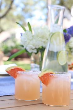 two glasses filled with drinks sitting on top of a wooden table next to a pitcher