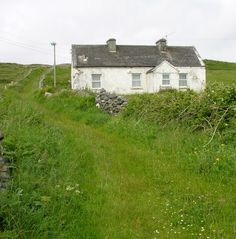 a white house sitting on the side of a lush green hillside next to a stone wall