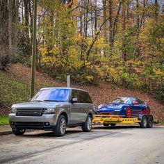 two cars that are parked next to each other on the side of the road with trees in the background