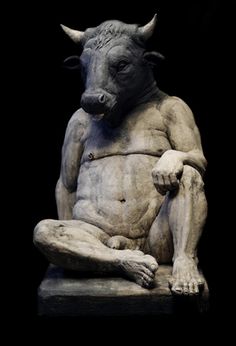 a statue of a bull sitting on top of a stone slab in front of a black background