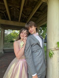 a young man and woman dressed in formal wear posing for a photo under a gazebo