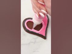 someone is decorating a heart shaped cookie with pink and brown icing on it