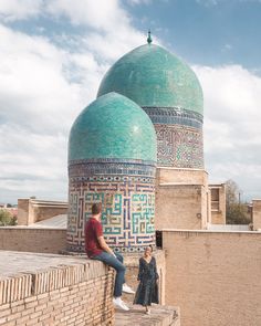 two people are sitting on the ledge of a wall near a building with blue domes