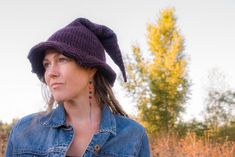 a woman wearing a denim jacket and a purple knitted hat is standing in a field