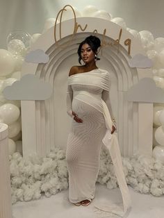 a pregnant woman standing in front of a backdrop with white balloons and clouds on it