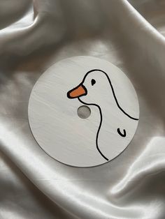 a white duck with an orange beak on a silver satin background that looks like it has been painted