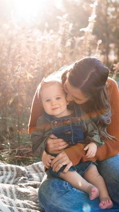 a woman holding a baby in her arms while sitting on a blanket with the sun shining down