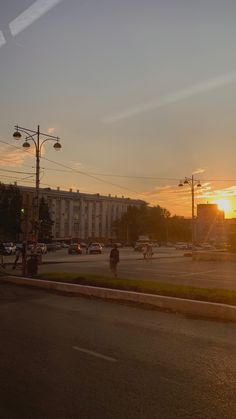 the sun is setting over a city street with cars and people walking on the sidewalk